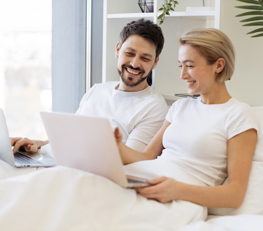 Junges Paar mit Laptops auf Bett sitzend